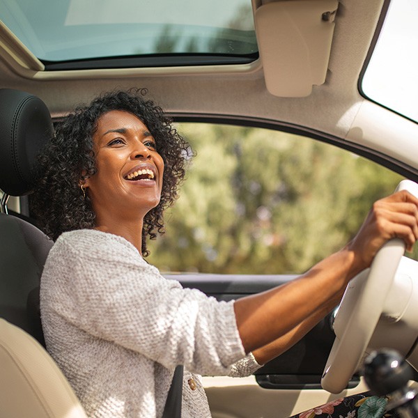 Woman behind the wheel of a car flashes a big smile as she gazes into the rearview mirror